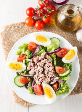 Domates, roka, ton balığı, yumurta, roka, kraker ve baharattan yapılmış taze balık salatası. Tahta arka planda beyaz bir kasede Sezar salatası.