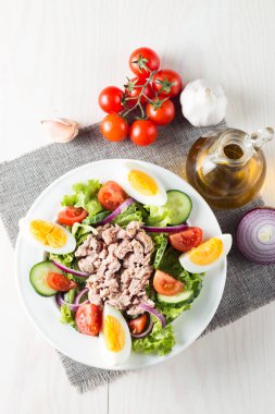 Domates, roka, ton balığı, yumurta, roka, kraker ve baharattan yapılmış taze balık salatası. Tahta arka planda beyaz bir kasede Sezar salatası.