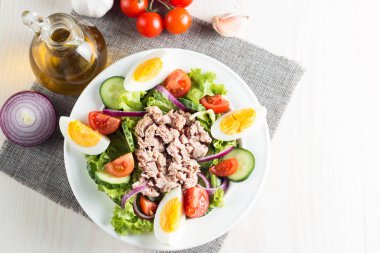 Domates, roka, ton balığı, yumurta, roka, kraker ve baharattan yapılmış taze balık salatası. Tahta arka planda beyaz bir kasede Sezar salatası.