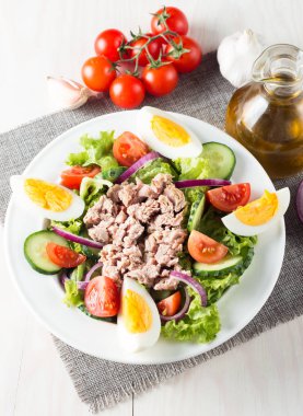 Domates, roka, ton balığı, yumurta, roka, kraker ve baharattan yapılmış taze balık salatası. Tahta arka planda beyaz bir kasede Sezar salatası.