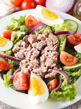 Domates, roka, ton balığı, yumurta, roka, kraker ve baharattan yapılmış taze balık salatası. Tahta arka planda beyaz bir kasede Sezar salatası.