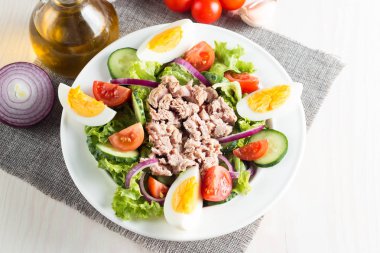 Domates, roka, ton balığı, yumurta, roka, kraker ve baharattan yapılmış taze balık salatası. Tahta arka planda beyaz bir kasede Sezar salatası.