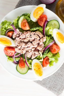 Domates, roka, ton balığı, yumurta, roka, kraker ve baharattan yapılmış taze balık salatası. Tahta arka planda beyaz bir kasede Sezar salatası.