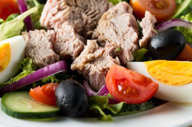 Domates, roka, ton balığı, yumurta, roka, kraker ve baharattan yapılmış taze balık salatası. Tahta arka planda beyaz bir kasede Sezar salatası.