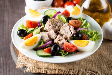 Domates, roka, ton balığı, yumurta, roka, kraker ve baharattan yapılmış taze balık salatası. Tahta arka planda beyaz bir kasede Sezar salatası.