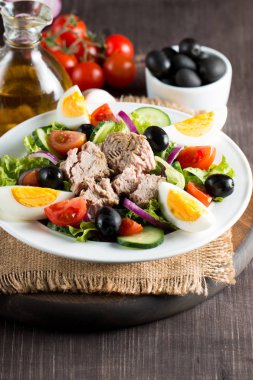 Domates, roka, ton balığı, yumurta, roka, kraker ve baharattan yapılmış taze balık salatası. Tahta arka planda beyaz bir kasede Sezar salatası.