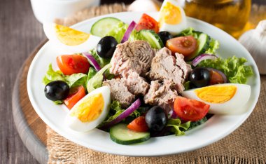 Domates, roka, ton balığı, yumurta, roka, kraker ve baharattan yapılmış taze balık salatası. Tahta arka planda beyaz bir kasede Sezar salatası.