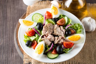 Domates, roka, ton balığı, yumurta, roka, kraker ve baharattan yapılmış taze balık salatası. Tahta arka planda beyaz bir kasede Sezar salatası.