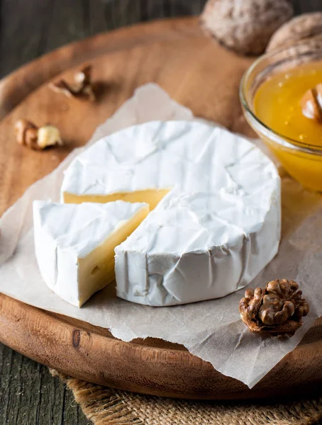 Brie type of cheese. Camembert cheese. Fresh Brie cheese and a slice on a wooden board with nuts, honey and leaves. Italian, French cheese.