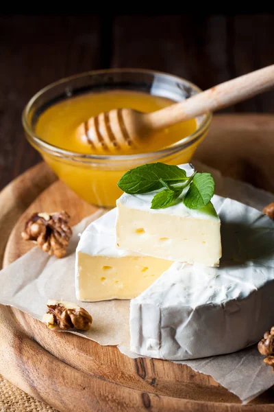 Brie type of cheese. Camembert cheese. Fresh Brie cheese and a slice on a wooden board with nuts, honey and leaves. Italian, French cheese.