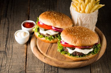 Ev yapımı Hamburger bira ile yakın çekim fotoğraf sığır eti, soğan, domates, marul, peynir ve baharat yaptı. Taze hamburger tatlı patates kızartması ve cips ile ahşap rustik tabloda.