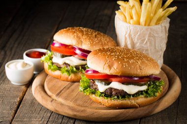 Ev yapımı Hamburger bira ile yakın çekim fotoğraf sığır eti, soğan, domates, marul, peynir ve baharat yaptı. Taze hamburger tatlı patates kızartması ve cips ile ahşap rustik tabloda.
