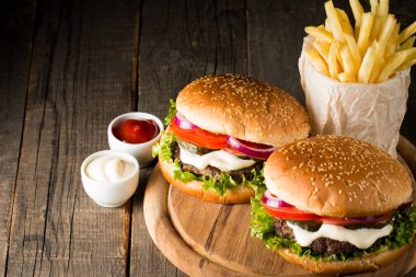 Ev yapımı Hamburger bira ile yakın çekim fotoğraf sığır eti, soğan, domates, marul, peynir ve baharat yaptı. Taze hamburger tatlı patates kızartması ve cips ile ahşap rustik tabloda.