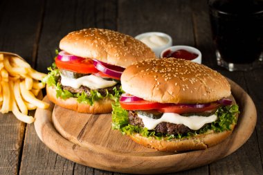 Ev yapımı Hamburger bira ile yakın çekim fotoğraf sığır eti, soğan, domates, marul, peynir ve baharat yaptı. Taze hamburger tatlı patates kızartması ve cips ile ahşap rustik tabloda.