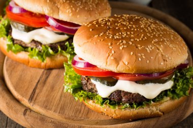 Ev yapımı Hamburger bira ile yakın çekim fotoğraf sığır eti, soğan, domates, marul, peynir ve baharat yaptı. Taze hamburger tatlı patates kızartması ve cips ile ahşap rustik tabloda.