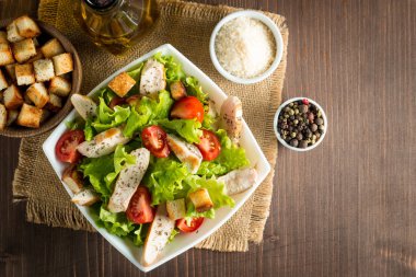 Taze salata domates, ruccola, tavuk göğsü, yumurta, roka, kraker ve baharat yapılmış. Ahşap arka plan üzerinde beyaz, şeffaf bir kasede Sezar salatası