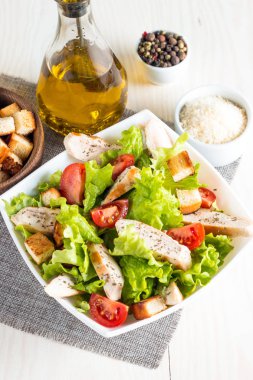 Taze salata domates, ruccola, tavuk göğsü, yumurta, roka, kraker ve baharat yapılmış. Ahşap arka plan üzerinde beyaz, şeffaf bir kasede Sezar salatası