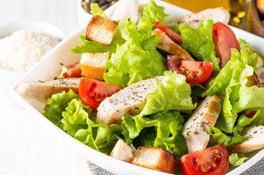 Taze salata domates, ruccola, tavuk göğsü, yumurta, roka, kraker ve baharat yapılmış. Ahşap arka plan üzerinde beyaz, şeffaf bir kasede Sezar salatası