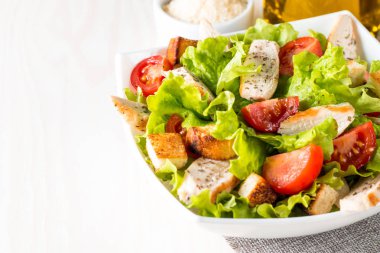 Taze salata domates, ruccola, tavuk göğsü, yumurta, roka, kraker ve baharat yapılmış. Ahşap arka plan üzerinde beyaz, şeffaf bir kasede Sezar salatası