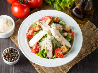 Taze salata domates, ruccola, tavuk göğsü, yumurta, roka, kraker ve baharat yapılmış. Ahşap arka plan üzerinde beyaz, şeffaf bir kasede Sezar salatası