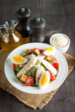 Taze salata domates, ruccola, tavuk göğsü, yumurta, roka, kraker ve baharat yapılmış. Ahşap arka plan üzerinde beyaz, şeffaf bir kasede Sezar salatası