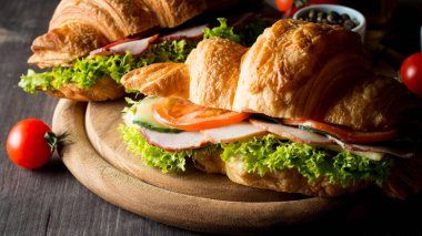 Taze kruvasan veya sandviç salata, jambon, jamon, jambon, salam, peynir, tavuk, domates ahşap arka plan ile. Sabah kahvaltı kavramı. Sağlıklı ve fast food.