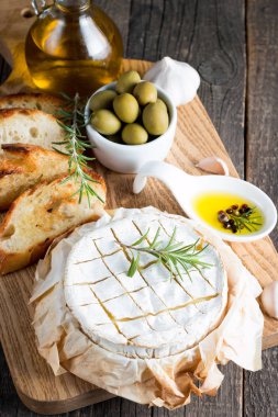Pişmiş camembert peyniri. Taze Brie peyniri ve bir dilim fındık, tatlım, biberiye ile ahşap bir gemide, baget ekmek ızgara tost ve yaprakları. Peynir Brie türü. İtalyan, Fransız peynir.