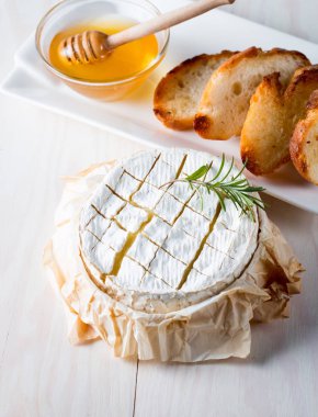 Pişmiş camembert peyniri. Taze Brie peyniri ve bir dilim fındık, tatlım, biberiye ile ahşap bir gemide, baget ekmek ızgara tost ve yaprakları. Peynir Brie türü. İtalyan, Fransız peynir.