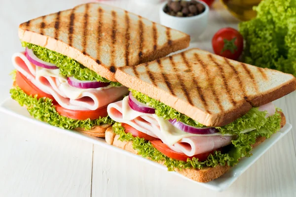 Close-up photo of a club sandwich. Sandwich with meat, prosciutto, salami, salad, vegetables, lettuce, tomato, onion and mustard on a fresh sliced rye bread on wooden background. Olives background.