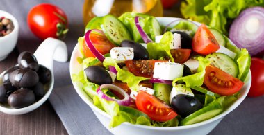 Kiraz domates, ruccola, roka, beyaz peynir, zeytin, salatalık, soğan ve baharat taze Yunan salatası yaptı. Sezar salatası ahşap arka plan üzerinde beyaz bir kase. Sağlıklı organik beslenme gıda kavramı.