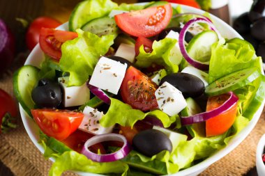 Kiraz domates, ruccola, roka, beyaz peynir, zeytin, salatalık, soğan ve baharat taze Yunan salatası yaptı. Sezar salatası ahşap arka plan üzerinde beyaz bir kase. Sağlıklı organik beslenme gıda kavramı.