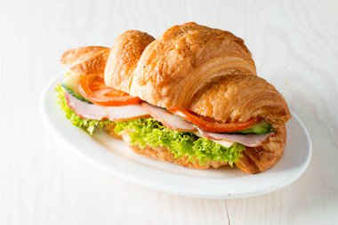 Taze kruvasan veya sandviç salata, jambon, jamon, jambon, salam, peynir, tavuk, domates ahşap arka plan ile. Sabah kahvaltı kavramı. Sağlıklı ve fast food.