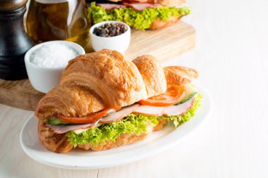 Taze kruvasan veya sandviç salata, jambon, jamon, jambon, salam, peynir, tavuk, domates ahşap arka plan ile. Sabah kahvaltı kavramı. Sağlıklı ve fast food.