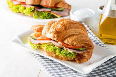 Taze kruvasan veya sandviç salata, jambon, jamon, jambon, salam, peynir, tavuk, domates ahşap arka plan ile. Sabah kahvaltı kavramı. Sağlıklı ve fast food.