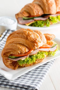 Taze kruvasan veya sandviç salata, jambon, jamon, jambon, salam, peynir, tavuk, domates ahşap arka plan ile. Sabah kahvaltı kavramı. Sağlıklı ve fast food.