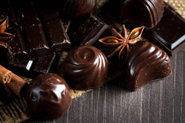 Koyu, beyaz ve sütlü çikolata yığını, cips çeşitleri. Kaba ahşap arka planda çikolata ve kahve çekirdekleri. Baharatlar, tarçın. Seçici makro odaklanma. Çikolata arkaplanı. Tatlılar