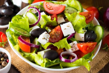 Kiraz domates, ruccola, roka, beyaz peynir, zeytin, salatalık, soğan ve baharat taze Yunan salatası yaptı. Sezar salatası ahşap arka plan üzerinde beyaz bir kase. Sağlıklı organik beslenme gıda kavramı.