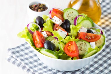 Kiraz domates, ruccola, roka, beyaz peynir, zeytin, salatalık, soğan ve baharat taze Yunan salatası yaptı. Sezar salatası ahşap arka plan üzerinde beyaz bir kase. Sağlıklı organik beslenme gıda kavramı.