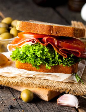 Club sandviç yakın çekim fotoğraf. Eti, jambon, salam, salata, sebze, marul, domates, soğan ve hardal ahşap arka plan üzerinde taze dilimlenmiş siyah ekmek üzerinde sandviç. Zeytin arka plan.