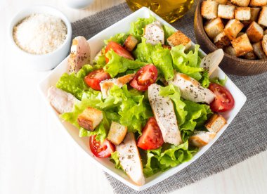 Taze salata domates, ruccola, tavuk göğsü, yumurta, roka, kraker ve baharat yapılmış. Ahşap arka plan üzerinde beyaz, şeffaf bir kasede Sezar salatası