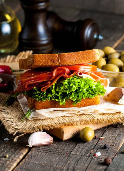 Close-up photo of a club sandwich. Sandwich with meat, prosciutto, salami, salad, vegetables, lettuce, tomato, onion and mustard on a fresh sliced rye bread on wooden background. Olives background.