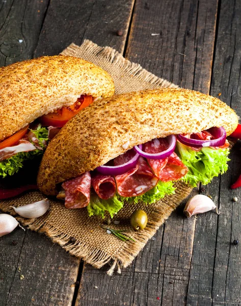 Close-up photo of a club sandwich. Sandwich with meat, prosciutto, salami, salad, vegetables, lettuce, tomato, onion and mustard on a fresh sliced rye bread on wooden background. Olives background.