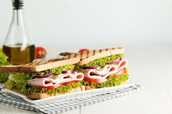 Close-up photo of a club sandwich. Sandwich with meat, prosciutto, salami, salad, vegetables, lettuce, tomato, onion and mustard on a fresh sliced rye bread on wooden background. Olives background.