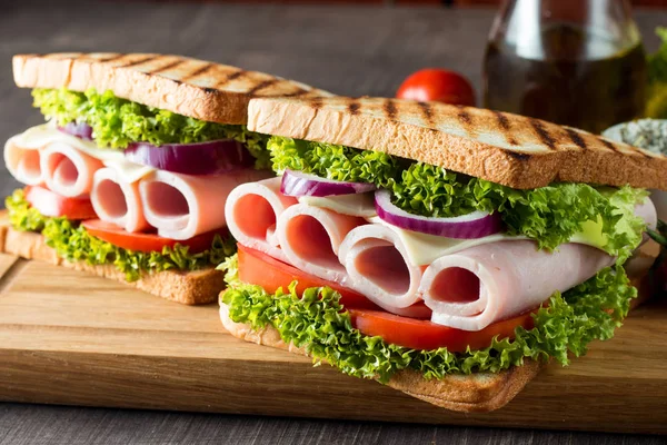 Close-up photo of a club sandwich. Sandwich with meat, prosciutto, salami, salad, vegetables, lettuce, tomato, onion and mustard on a fresh sliced rye bread on wooden background. Olives background.