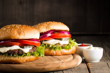 Ev yapımı Hamburger bira ile yakın çekim fotoğraf sığır eti, soğan, domates, marul, peynir ve baharat yaptı. Taze hamburger tatlı patates kızartması ve cips ile ahşap rustik tabloda.