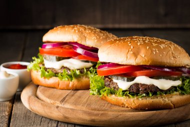 Ev yapımı Hamburger bira ile yakın çekim fotoğraf sığır eti, soğan, domates, marul, peynir ve baharat yaptı. Taze hamburger tatlı patates kızartması ve cips ile ahşap rustik tabloda.