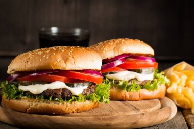 Ev yapımı Hamburger bira ile yakın çekim fotoğraf sığır eti, soğan, domates, marul, peynir ve baharat yaptı. Taze hamburger tatlı patates kızartması ve cips ile ahşap rustik tabloda.