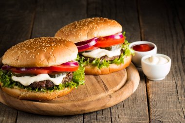 Ev yapımı Hamburger bira ile yakın çekim fotoğraf sığır eti, soğan, domates, marul, peynir ve baharat yaptı. Taze hamburger tatlı patates kızartması ve cips ile ahşap rustik tabloda.