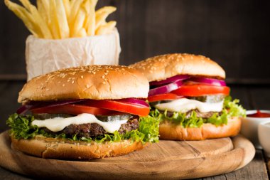 Ev yapımı Hamburger bira ile yakın çekim fotoğraf sığır eti, soğan, domates, marul, peynir ve baharat yaptı. Taze hamburger tatlı patates kızartması ve cips ile ahşap rustik tabloda.