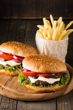 Ev yapımı Hamburger bira ile yakın çekim fotoğraf sığır eti, soğan, domates, marul, peynir ve baharat yaptı. Taze hamburger tatlı patates kızartması ve cips ile ahşap rustik tabloda.